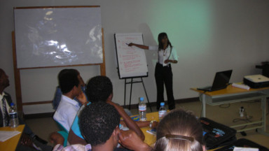 A woman stands in a classroom pointing to a flipchart
