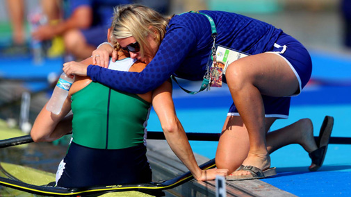 Sarah-Jane McDonnell kneels at the edge of the water to hug rower Sanita Puspure